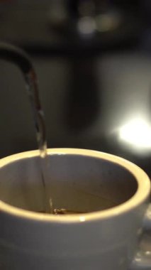 Siyah kafe tezgahında sıcak kahve yapmak için bir bardağa sıcak su döken birine yaklaş.