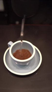Siyah kafe tezgahında sıcak kahve yapmak için bardağa sıcak su döken biri.