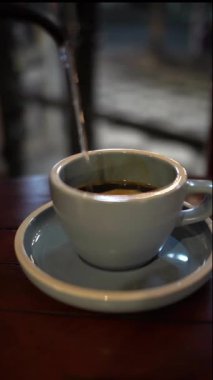 Sıcak kahve yapmak için bir bardağa sıcak su döken birine yaklaş.