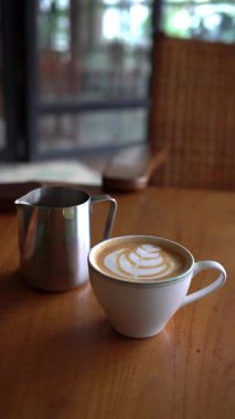 Bir fincan köpüklü latte ve ahşap masada bir kavanoz.