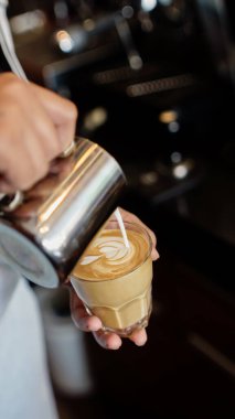 Barista bir bardak sıcak latte üzerinde latte yapıyor.