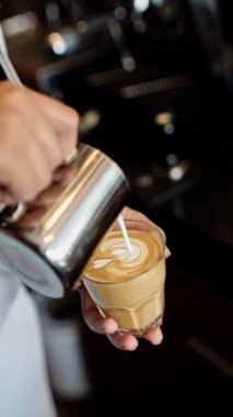 Barista bir bardak sıcak latte üzerinde latte yapıyor.