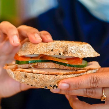 Kapalı kadın sandviç tutuyor ve yiyor.