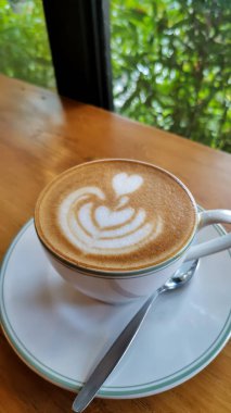 Masada köpüklü bir fincan sıcak latteyi kapat.