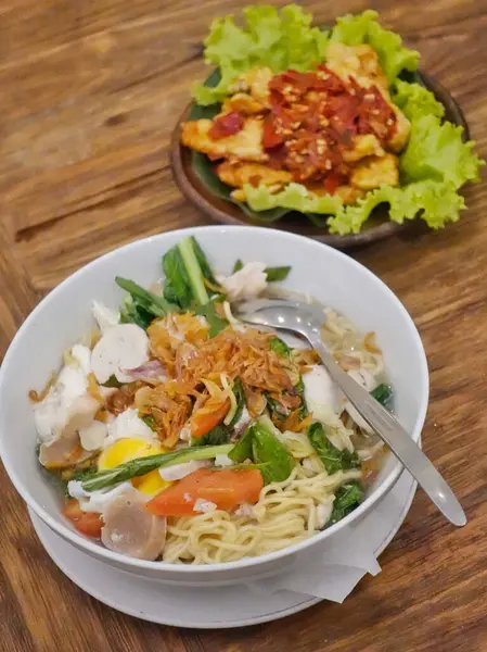 Üzerinde sebzeler, dilimler, haşlanmış yumurta ve gevrek arpacık soğanları olan bir erişte çorbası tabağı.