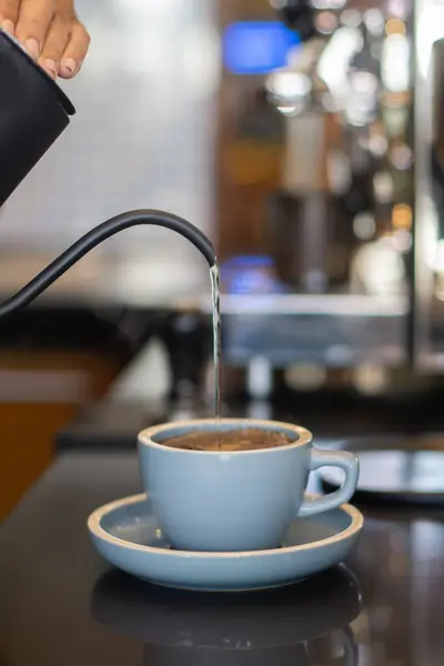 Sıcak kahve yapmak için tezgahın üstündeki fincana sıcak su dökmek.