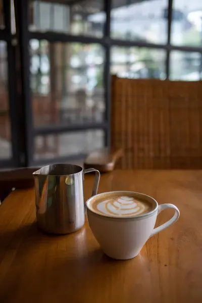 Bir fincan köpüklü latte ve ahşap masada bir kavanoz.