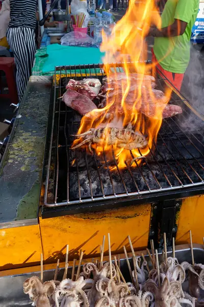 Açık havada kalamar ve sığır eti de dahil olmak üzere çeşitli etleri pişiren canlı alevlerle dolu bir ızgara.