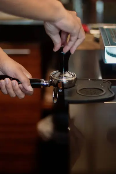 Bir insan kahve makinesinin bir parçası olan portafilterdeki kahve telvelerini bastırmak için kahve değiştirici kullanır. Tezgah ve yakınlardaki ekipmanlarla gösterilen profesyonel ya da ev yapımı bir espresso istasyonu gibi görünüyor..