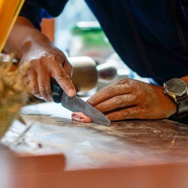 Ev yapımı pembe makarna yapıyorum. Ahşap bir yüzeyde hamuru un tozuyla küçük parçalara ayıran eller. Bir bıçak, eşit büyüklükte parçaları dilimlemek için kullanılıyor. Arka plan bulanık, bu da mutfak düzeneği olduğunu gösteriyor..