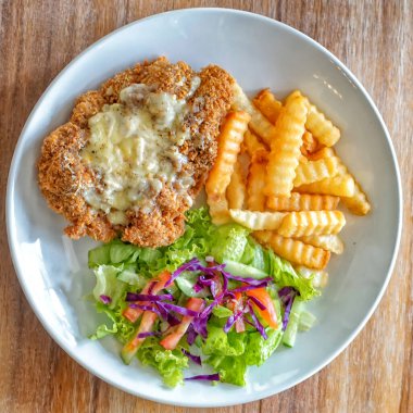 Kızarmış patates kızartması ve beyaz tabakta salata ile Parmigiana usulü tavuk manzarası. Kremalı sosla kaplanmış fırında tavuk pirzolası yarım tabak beyaz tabak ve taze yeşil yapraklı salata dilimlenmiş domates, kırmızı lahana ve salatalık içerir.