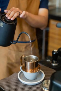 Bir insan, siyah bir çaydanlıktan Vietnam damlayan kahve filtresine sıcak su döker. Metal filtre, bir kapağı ve altında delikleri ile, bir seramik fincan ve fincan üzerinde oturur