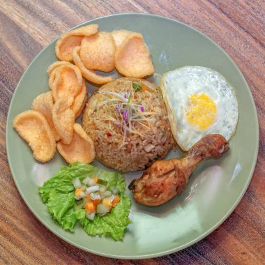 Ortasında çıtır karides krakerleriyle çevrili filizlerle süslenmiş kızarmış pirinçli bir tabak. Yanında da güneşli bir yumurta, kızarmış tavuk budu ve salatalık yaprağının üstünde küçük bir porsiyon turşu.