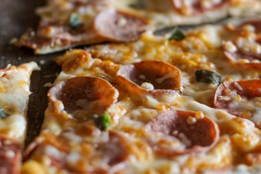 Biber dilimleri ve erimiş peynirle kaplı bir pizzanın yakın çekimi. Kabuk ince ve çıtır çıtır görünürken, peynir altın renginde ve hafifçe kahverengidir. Görünür yeşil bitkiler renk katar, dokuyu ve cazibeyi arttırır.