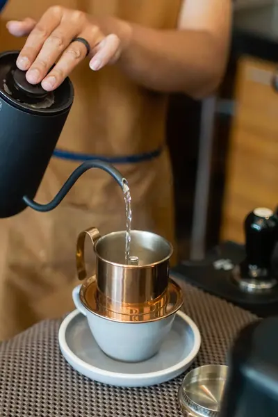 Bir insan, siyah bir çaydanlıktan Vietnam damlayan kahve filtresine sıcak su döker. Metal filtre, bir kapağı ve altında delikleri ile, bir seramik fincan ve fincan üzerinde oturur