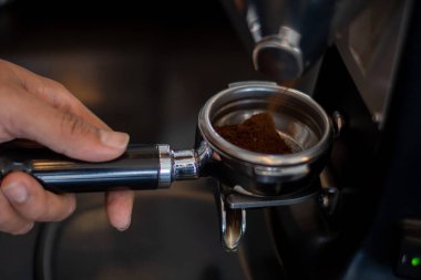 Bir el kahve öğütücüsünün altında bir iskele filtresi tutuyor, taze öğütülmüş kahve yakalıyor. Metal portafilter, espresso makinesinde kullanılmak üzere tasarlanmış bir sapla daireseldir.