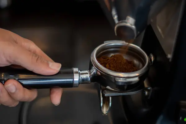 Bir el kahve öğütücüsünün altında bir iskele filtresi tutuyor, taze öğütülmüş kahve yakalıyor. Metal portafilter, espresso makinesinde kullanılmak üzere tasarlanmış bir sapla daireseldir.