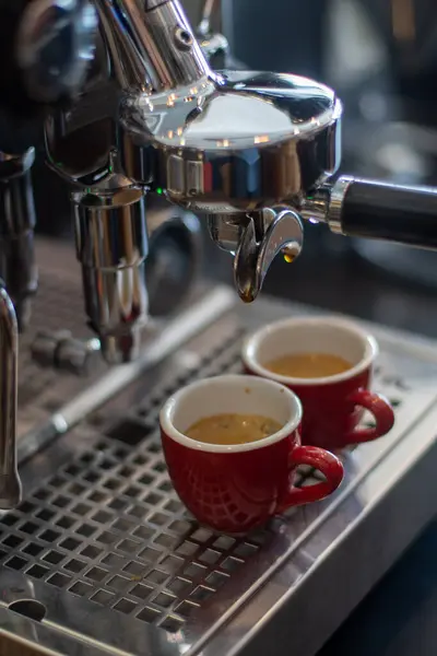 İki kırmızı seramik fincan, serin, paslanmaz çelik espresso makinesinin damlalarının üzerinde, taze demlenmiş kahve topluyor.