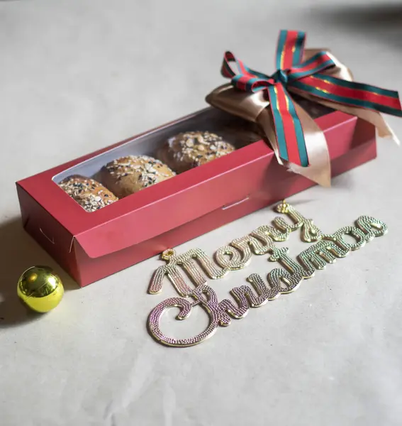 Noel hediyesi kutusunda üzerinde tohumlar olan fırınlanmış çörekler var. Büyük bir altın, kırmızı ve yeşil kurdeleyle süslenmiş. Hafif bir arkaplanda 