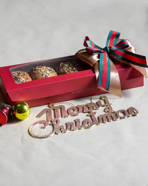 Noel hediyesi kutusunda üzerinde tohumlar olan fırınlanmış çörekler var. Büyük bir altın, kırmızı ve yeşil kurdeleyle süslenmiş. Hafif bir arkaplanda 