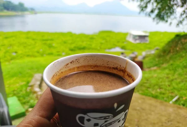 A cup of hot coffee on a cold day, with a lake and mountains in the background