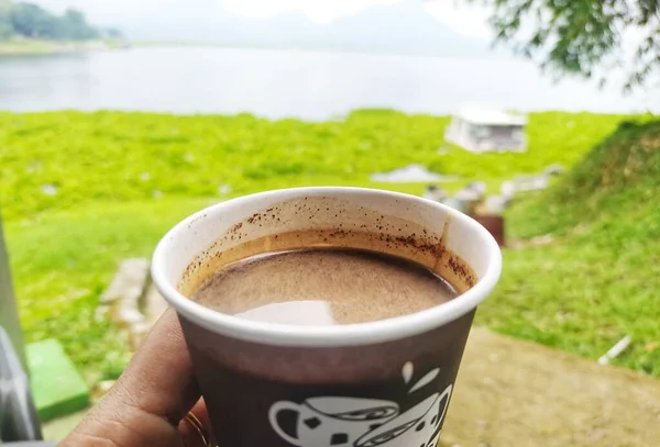 A cup of hot coffee on a cold day, with a lake and mountains in the background