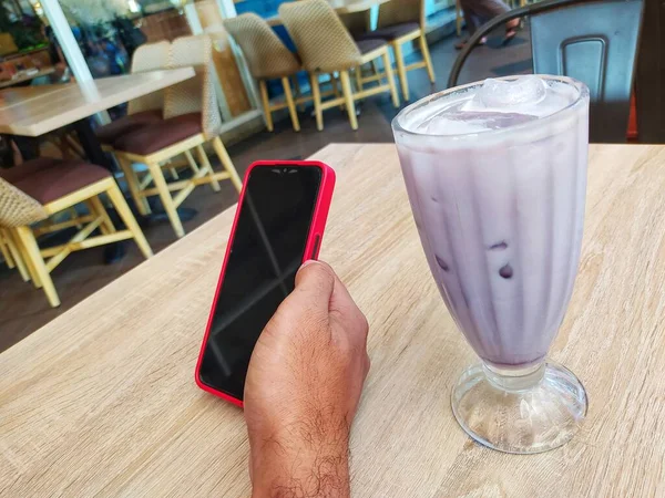 Ręce Trzymające Smartfona Szklanką Lodowego Taro Milkshake Krzesła Stołowe Kawiarni — Zdjęcie stockowe