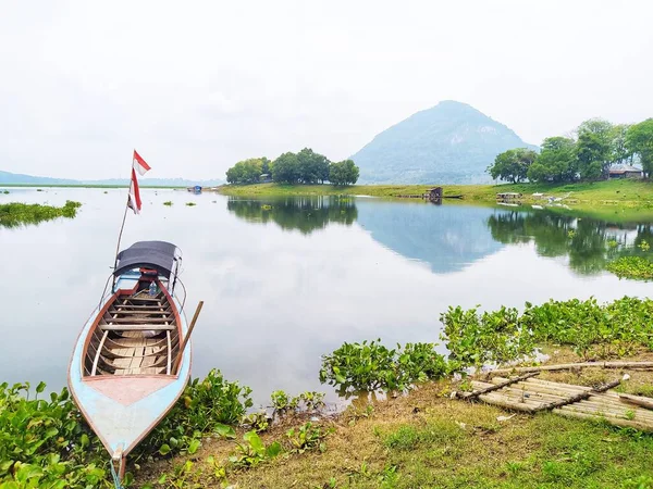 stock image A very beautiful lake view with a mountain background, water hyacinth plants on the surface of the lake and fish farmer boats on the shore