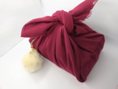 Kırmızı bir beze sarılmış bir hediye. Beyaz kabarık bir top askısı ile süslenmiş. Doğum günü hediyeleri. Beyaz bir arkaplanda izole edilmiş.