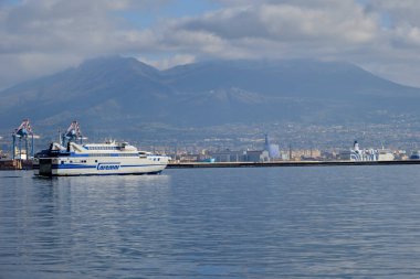 A ship in the foreground as it leaves the Port of Naples. In the background you can see Monte Somma on the right and Vesuvius in the centre, with its summit covered by clouds.