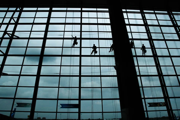 A silhouette of a worker cleaning windows hangs from a rope in the airport building.