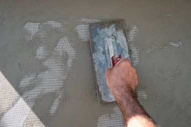 İşçi duvarı alçılamak için duvara bir mala çimento koyuyor.