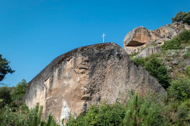 Tepenin ortasında, tepesinde metalik bir haç olan dev bir kaya.
