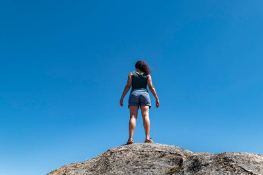 Etrafındaki manzaranın tadını çıkarırken bir kayanın tepesinde dinlenen bir kadın.