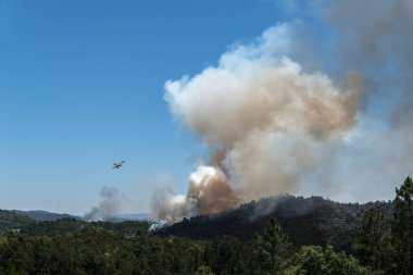 Su taşıyan uçaklar büyük bir beyaz ve siyah duman bulutu bırakan orman yangınıyla savaşmak için.