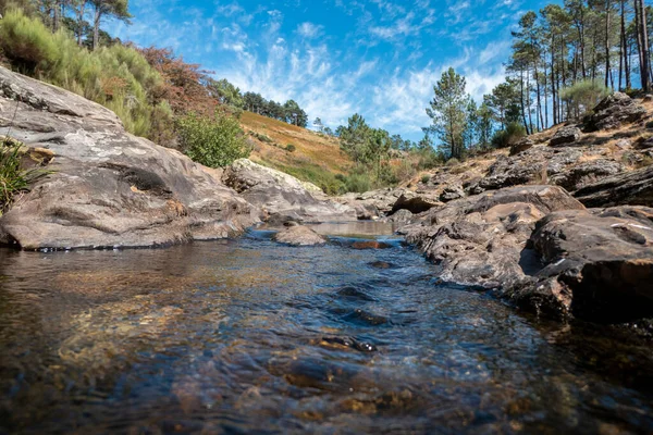 Stock image Between mountains and large rocks a stream of water flowing down the mountain at Fisgas de Ermelo in Serra do Alvao in Portugal on a day with some clouds in the sky