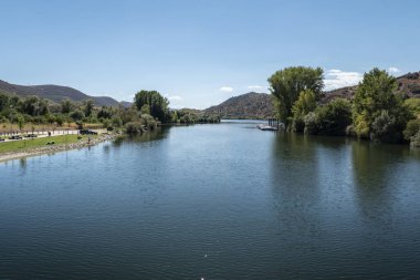 Foz do Sabor köyüne yakın bir nehir, solunda bir park, sağında bir rıhtım ve arkasında Portekiz 'de dağlar var.