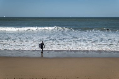 Sörfçü sörf tahtasıyla dalgaları yakalamaya hazırlanıyor. Arka planda daha çok sörfçü var.