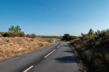 Portekiz 'de mavi gökyüzü gününde etrafında bazı kıvrımlar ve araziler olan bir yol.