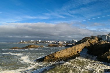 Biarritz şehrinin bir kısmının panoramik manzarası, önünde kumsal, önünde kayalar ve güçlü bir deniz kabarması var.