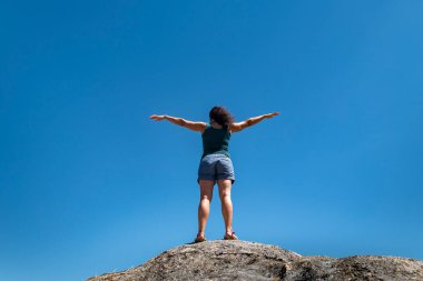 Etrafındaki manzaranın tadını çıkarırken, bir kayanın tepesinde kolları açık turist bir kadın neşe ve barışın simgesi olarak.