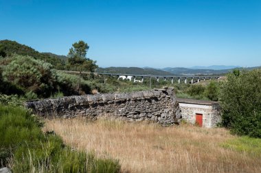 Taş su kemeri diğer zamanlarda su getirmek için aşağıdaki değirmene tahıl öğütmek için, bir ormanın ortasında ve arka planda bir köprü