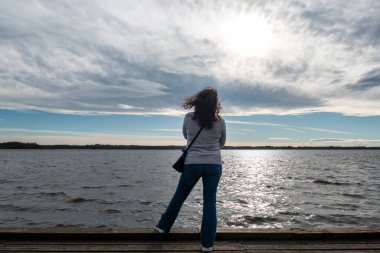 Rıhtımdaki turist kadın bulutlu bir günde Fransa 'nın Bask bölgesinde Azur Gölü' nün tadını çıkarıyor.
