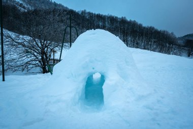 Small house made of snow in the middle of the mountain and forests on a cold winter day