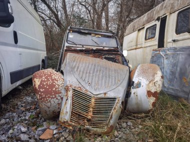 Abandoned and rusty classic car in the middle of other cars in the same situation, for parts or scrapping