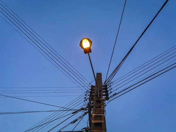 In the middle of many wires, a street light pole lit up at night