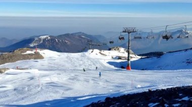 Panoramic video with a snow slope and some skiers going down the mountain while the cable car goes up with more skiers to the top in Pierre Saint Martin in the Pyrenees, France