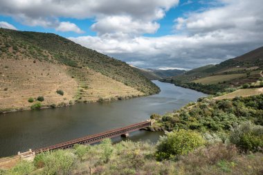 Tepeler ve dağlar arasında ve parçalı bulutlu bir günde, Douro nehrinin ağzında demir bir çizgi olan metalik bir köprü ve Portekiz 'in Tras Montes şehrinde Coa nehri arasında