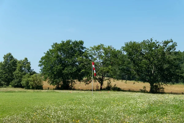 Dönen koni rüzgarın yönünü gösteriyor. Bazı ağaçların ve yeşil çimenlerin ortasında paraşütle atlamak için bir iniş alanına yerleştirilmiş.