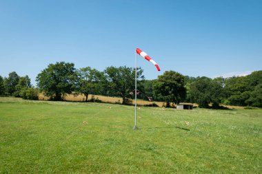 Dönen koni rüzgarın yönünü gösteriyor. Bazı ağaçların ve yeşil çimenlerin ortasında paraşütle atlamak için bir iniş alanına yerleştirilmiş.